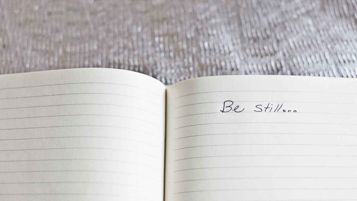 white pages of a ruled notebook with the words be still written on the page.